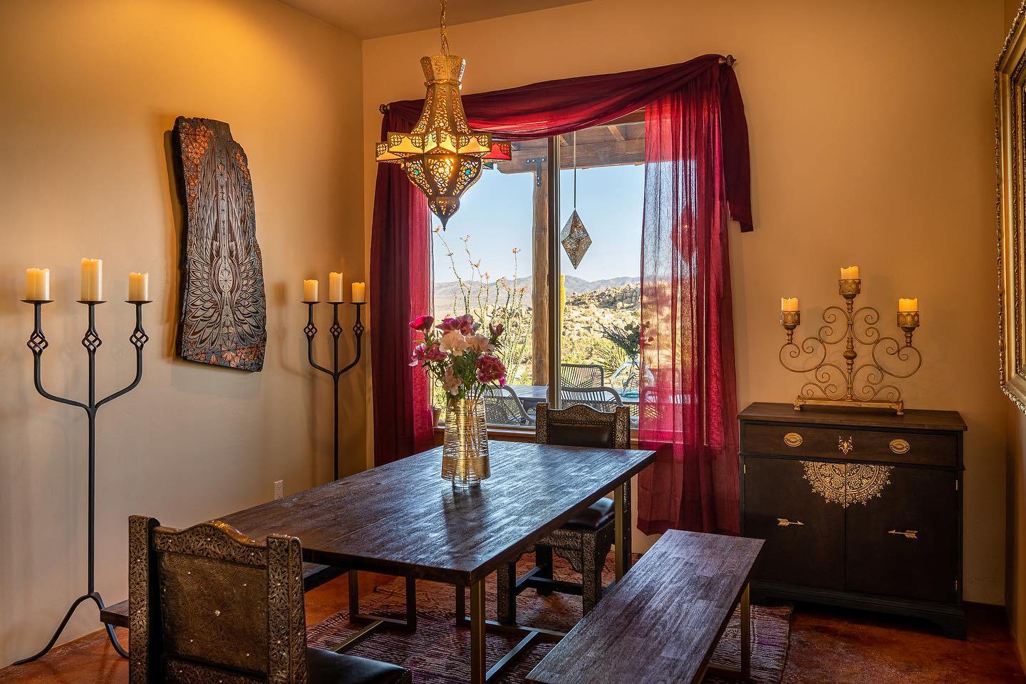Interior of the Boulder Horizons Joshua Tree rental: Moroccan dining room with brass chandelier, candelabras, and a window framing the desert