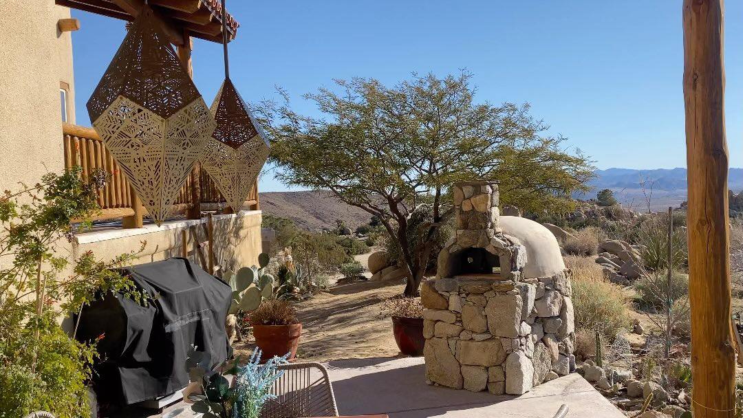Hand-built stone wood-fired pizza oven on the patio with brass lanterns and desert views
