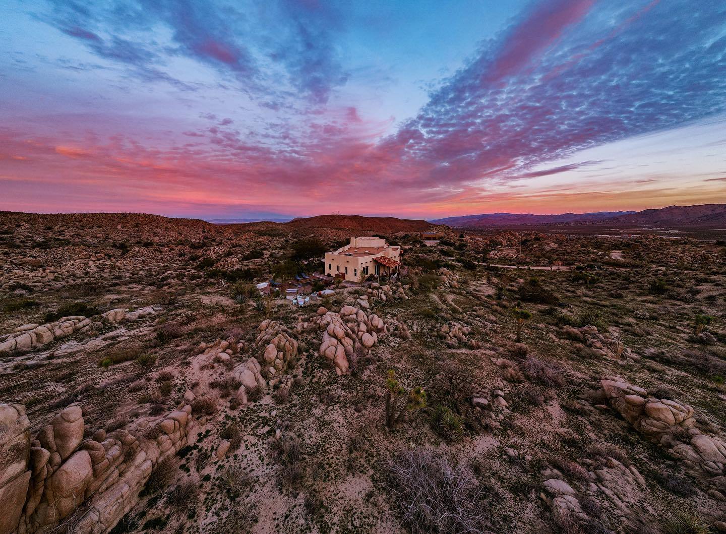 Aerial dusk view over Yucca Valley boulder fields with the Boulder Horizons estate glowing under a pink and blue sky