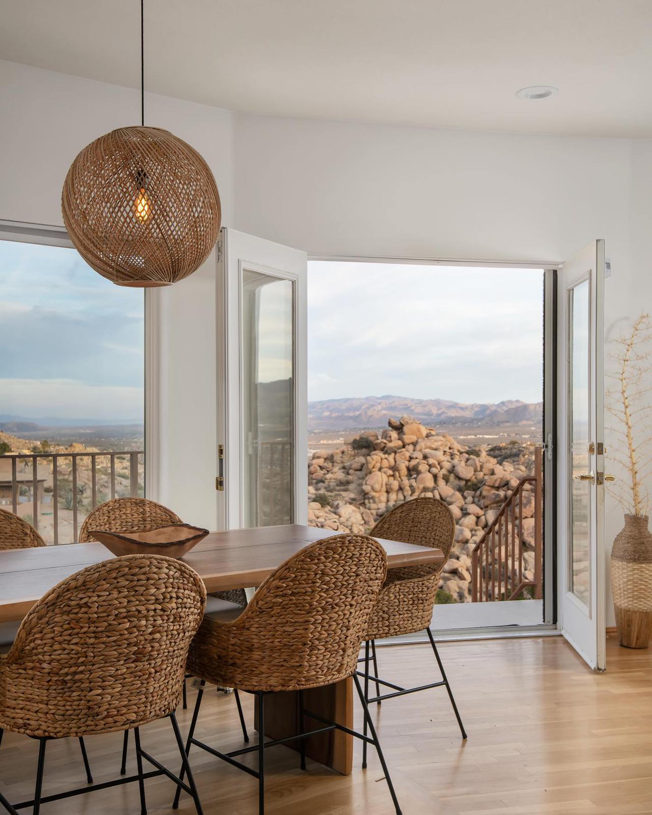 Interior dining nook with rattan chairs and French doors opening onto hilltop boulders at this Yucca Valley rental